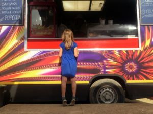 Small girl in front of food truck with colorful vehicle wrap